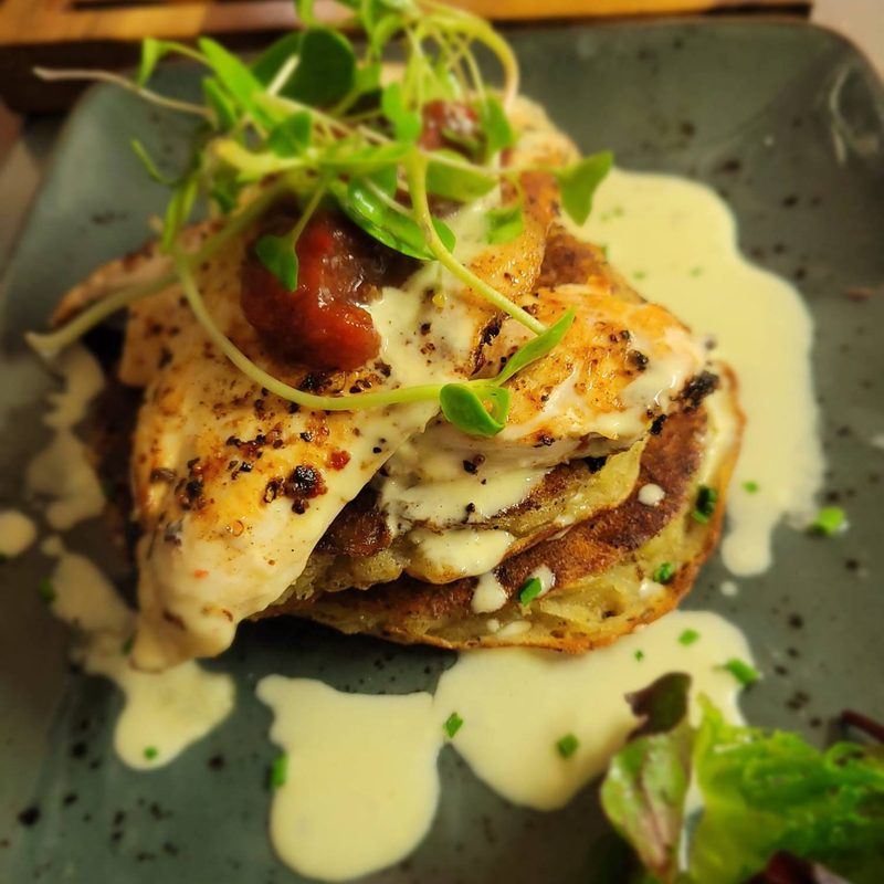 A potato pancake stack with fish, sauce, relish and pea shoots